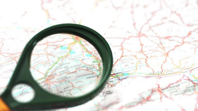 Hand holding magnifying glass over map for research and travel planning.