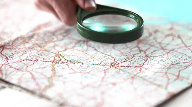 Hand holding magnifying glass over map for research and travel planning.