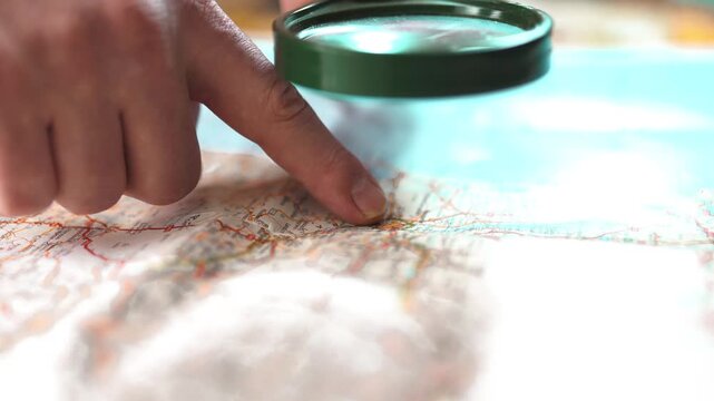 Hand holding magnifying glass over map for research and travel planning.