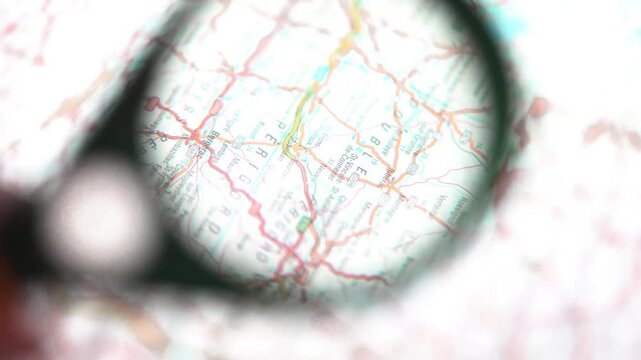 Hand holding magnifying glass over map for research and travel planning.