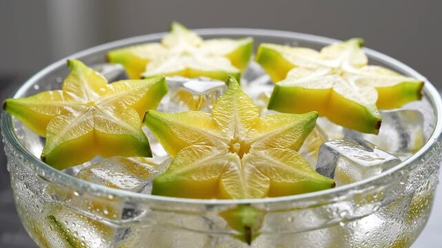 Hand adding ice cube to star fruit slices in glass bowl