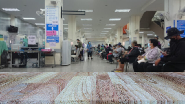 Empty wooden table top with blurred background of patients waiting to see doctor in hospital or clinic. Mock up for display of health and medical products.