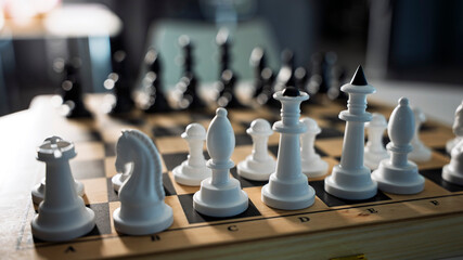 Classic wooden chessboard with black and white plastic pieces on a white round table. Strategic game setup in bright sunlight, perfect for logic, competition, education, and leisure concepts. © Alisa