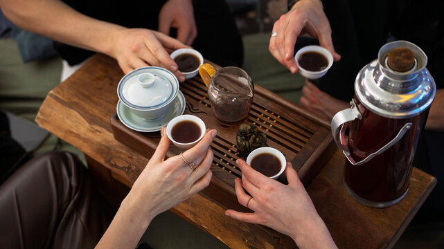 A man pouring hot water from a vintage red thermos into a white gaiwan during a traditional Chinese tea ceremony. Steam rises from the cup on a wooden table. Authentic oriental tea brewing process.