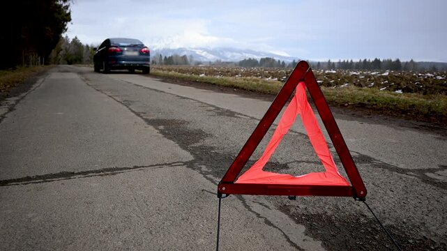 Red warning triangle indicating a car breakdown on a rural road with mountains in the background