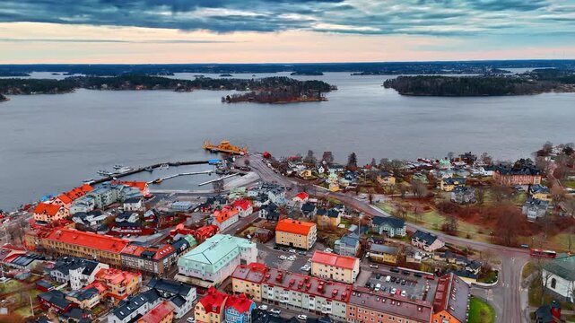 Footage over the town with bright roofs in the scenery. Dark clouds gathered in the sky over the islets in the backdrop. Aerial view.