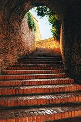 Fototapeta premium Brick staircase leading through arched tunnel toward daylight, representing transition, progress, hope, and passage from darkness to light.