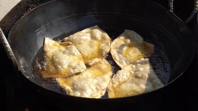 Samosas frying in hot oil in a traditional karahi
