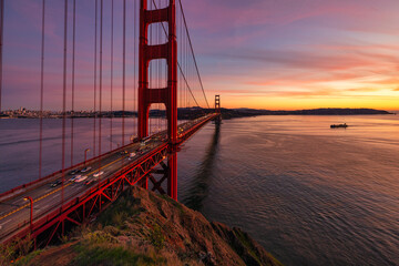 Obraz premium Golden Gate Bridge at sunset in San Francisco with long exposure light trails and vibrant pink sky reflecting over calm bay waters