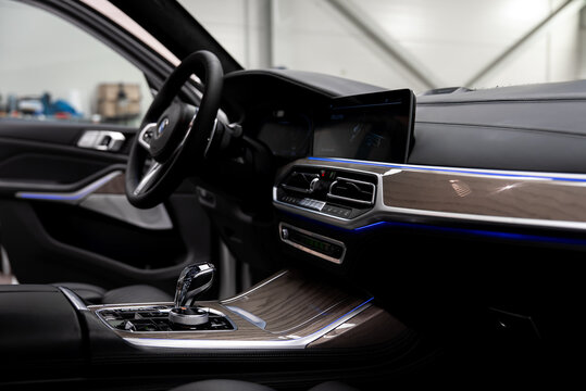 Interior view of a white BMW X7 shows cockpit and center console, crystal gear selector, iDrive controller, widescreen display, hexagonal vents, and ambient LED lighting.