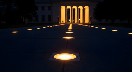 Obraz premium A series of glowing circular ground lights beautifully illuminate a grand pathway leading directly towards an impressive building at night.