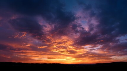 Fototapeta premium Vibrant sunset clouds over a dark silhouetted landscape at dusk