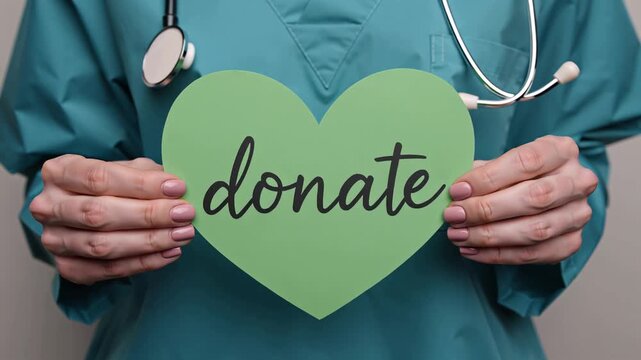 The doctor's hands hold a paper sign in the shape of a heart with the inscription "Donat"