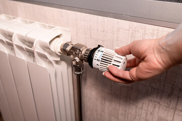 Female Hand Adjusting White Radiator Thermostat Valve to Control Temperature and Save Energy at Home