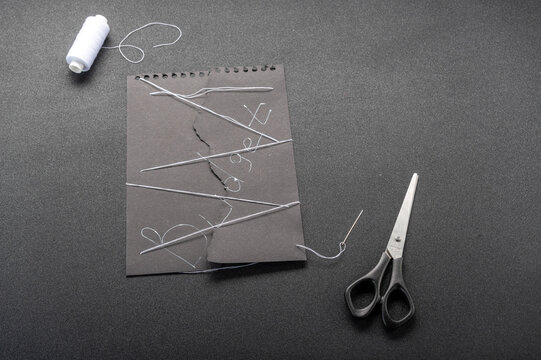 Broken budget concept. Torn black paper with Budget word sewn together with white threads on black background.