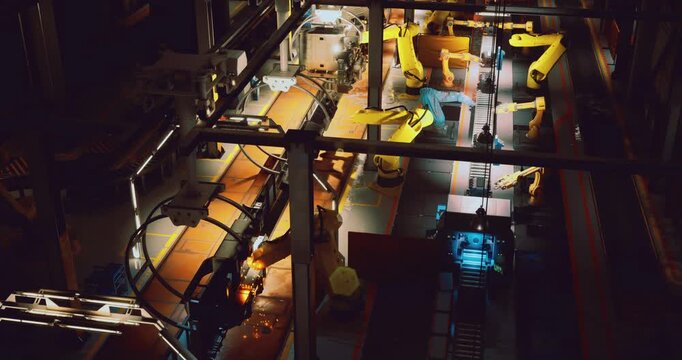 A view from above shows yellow robotic arms working on an assembly line in a manufacturing facility during the night.