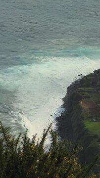 Scenic coastal highway beneath steep green cliffs and crashing Atlantic waves