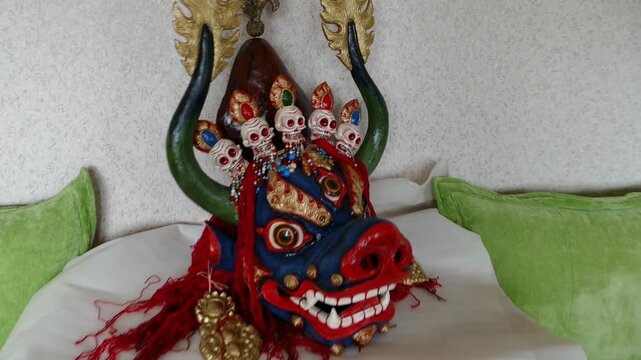 A large blue Mongolian mask of a angry Buddhist deity. Chojal is the god of death. It is depicted with a bull's head, three eyes and a crown of five human skulls.