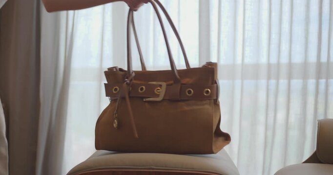 A brown purse is sitting on a chair in front of a window