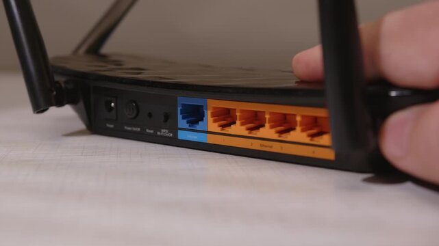 Man's hand pulls out wired internet cable from Wi-Fi router slot and inserts it