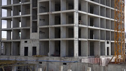 Fototapeta premium Unfinished reinforced concrete building frame at a construction site with a yellow crane.