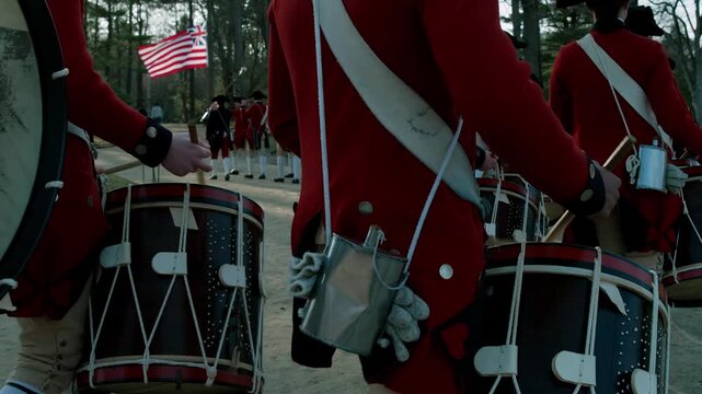 Revolutionary War soldiers in red coats marching with drums and a flag