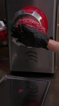 A meat grinder grinds minced meat at a meat processing plant. Hands of a worker