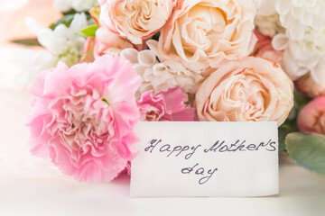 Beautiful bouquet of blush roses and pink carnations with white chrysanthemums and green leaves, greeting card with handwritten happy mothers day message, soft light background, celebration concept 