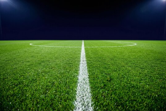 Empty football field at night with illuminated stadium lights and green grass center line