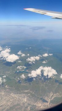 Airplane wing and cloudscape moving over green mountainous terrain with river and small lake on a sunny day