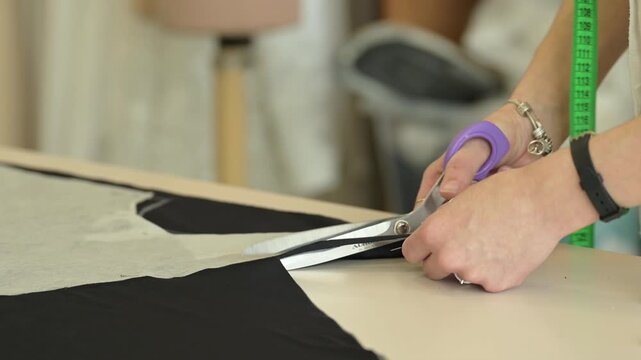 Seamstress cuts fabric pieces with scissors on a work table in a studio