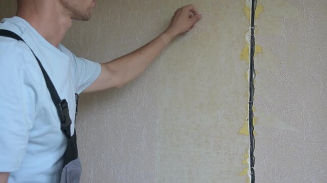 Man repairs wall surface, applying adhesive to damaged area in indoor setting