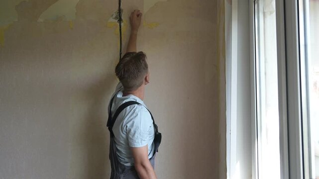Man prepares wall for painting, applying primer with roller in bright room
