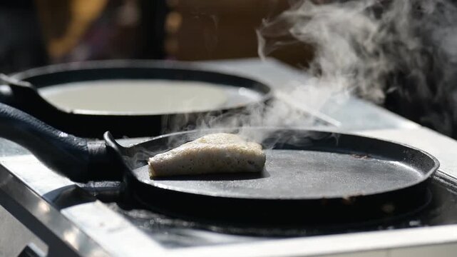 Cooking process of food on hot griddle with steam rising in outdoor setting