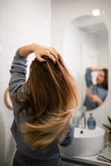 Naklejka premium Young woman caring for long brown hair in bathroom