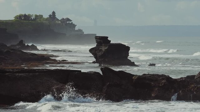 Tanah lot temple,Moody Coastline With Rolling Waves, Overcast Sky And Dramatic Clouds, Rocky Foreground With Distant Temple Pagoda, Cinematic Documentary Travel Vibe And Textured Seascape.