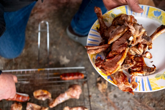 A person prepares assorted meats, including ribs and sausages