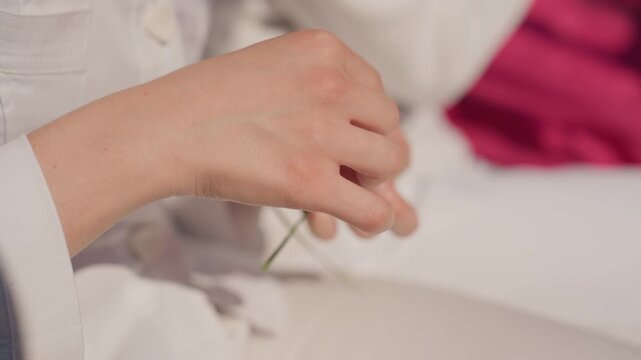 Closeup hands tying grass knot caucasian bridesmaid on soft couch preparing small token for family marriage, pink cushion background, steady fingers, slow calming ritual before ceremony