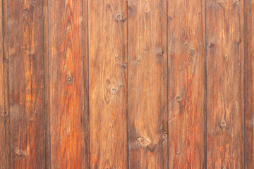 Close-up view of a rustic wooden wall featuring vertical planks with varying shades of brown and visible grain patterns, creating a warm and natural texture