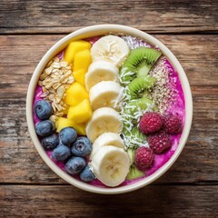 Colorful smoothie bowl topped with banana, kiwi, mango, berries, oats and seeds on rustic wooden table.