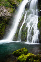 Fototapeta premium Long‑Exposure Waterfall Flowing Over Mossy Rocks in a Forest with Soft Light and Natural Atmosphere