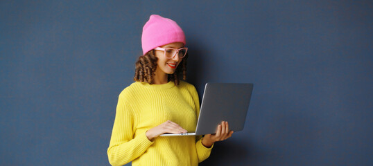 Happy modern young woman working on laptop, freelancer girl looking at computer in colorful clothes