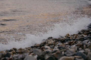 Obraz premium Waves crashing on rocky shore at sunset, water splashing on pebbles