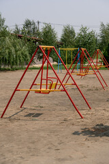 Colorful swings in playground surrounded by trees on sunny day
