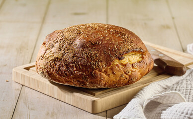 Fresh homemade sweet and sour rye bread with caraway seeds on cutting board with knife on light wooden table