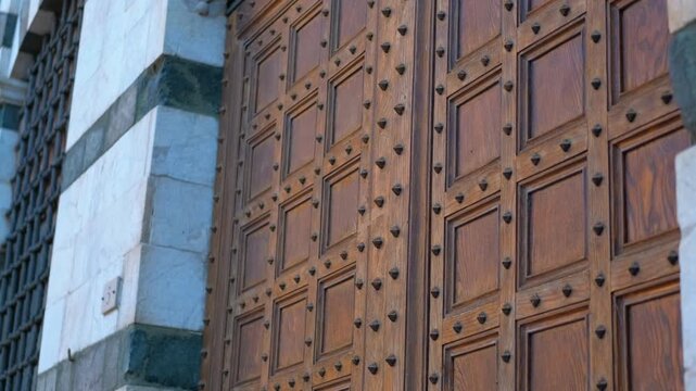 Ancient wooden door with metal studs in perspective. Sunlight illuminates an ancient, imposing wooden door adorned with metal studs, showcasing its intricate details and historical significance
