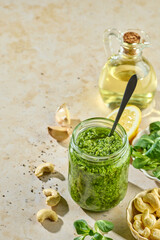 Fresh homemade green sprout pesto in glass jar on sunny kitchen table with ingredients