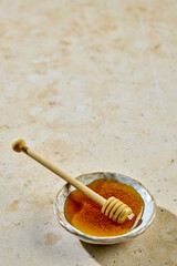 Fresh honey in small ceramic bowl with wooden spoon on sunny kitchen table with copy space