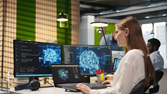 IT expert in high tech startup office uses neural networks to develop artificial intelligence models. Female engineer uses AI to run tasks across devices, monitoring progress on screens, camera A