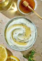 Greek yogurt bowl with honey and spices on sunny kitchen table with ingredients, top view